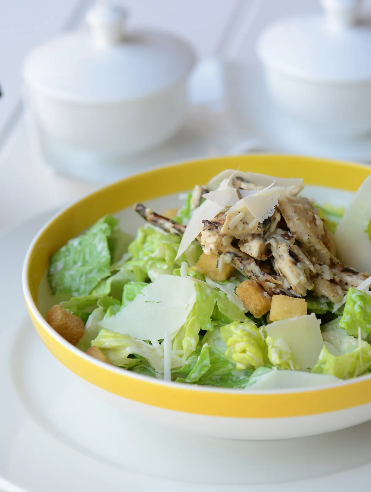 Chicken Caesar salad with parmesan shavings and croutons in a yellow-rimmed bowl — professional food photographer Dubai