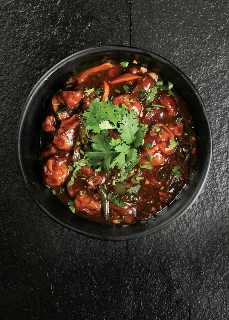 Glazed Indo-Chinese chicken garnished with coriander in a black bowl — hotel food photographer in Dubai