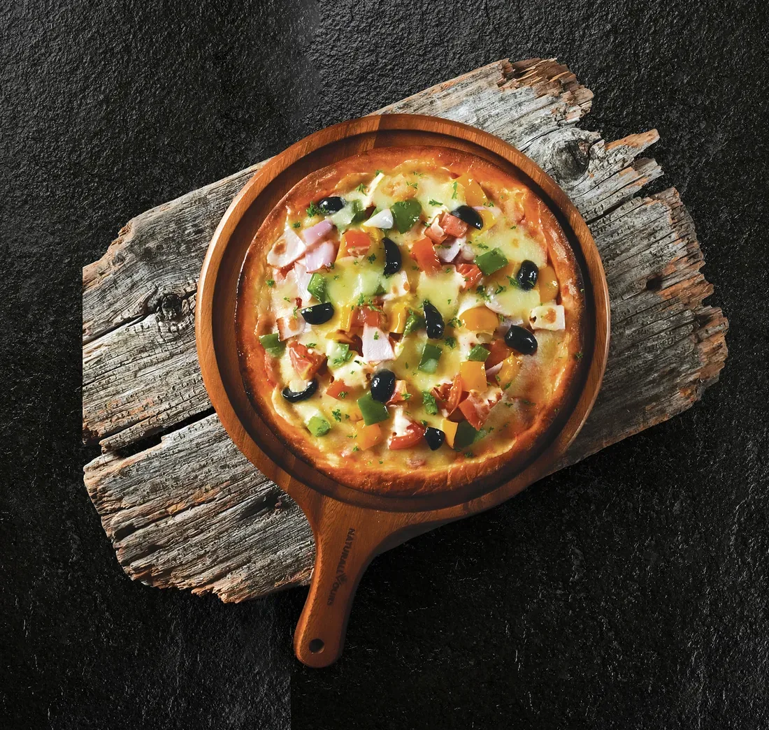 Pizza with olives and bell peppers on a wooden paddle and rustic board — restaurant food photography Dubai