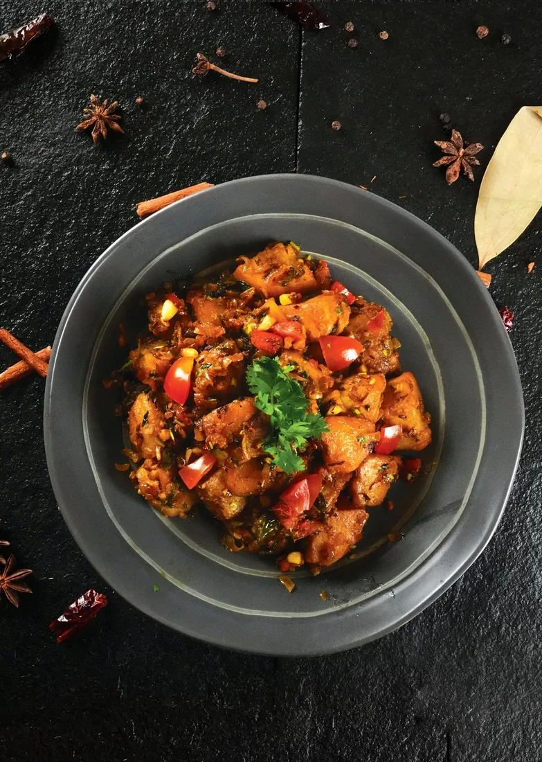 Overhead spiced chicken stir-fry with whole spices on dark slate — Dubai food photographer