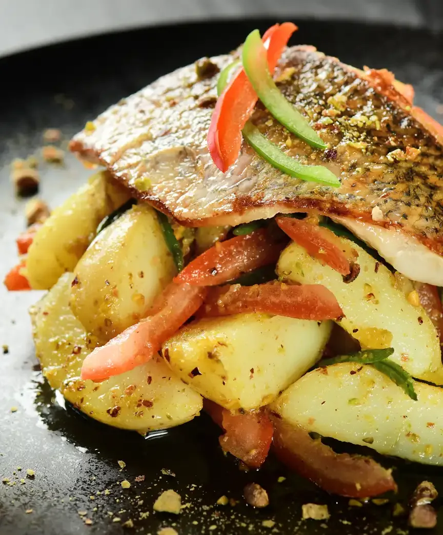 Pan-seared fish fillet served over spiced potatoes and peppers, fine-dining food photography in Riyadh
